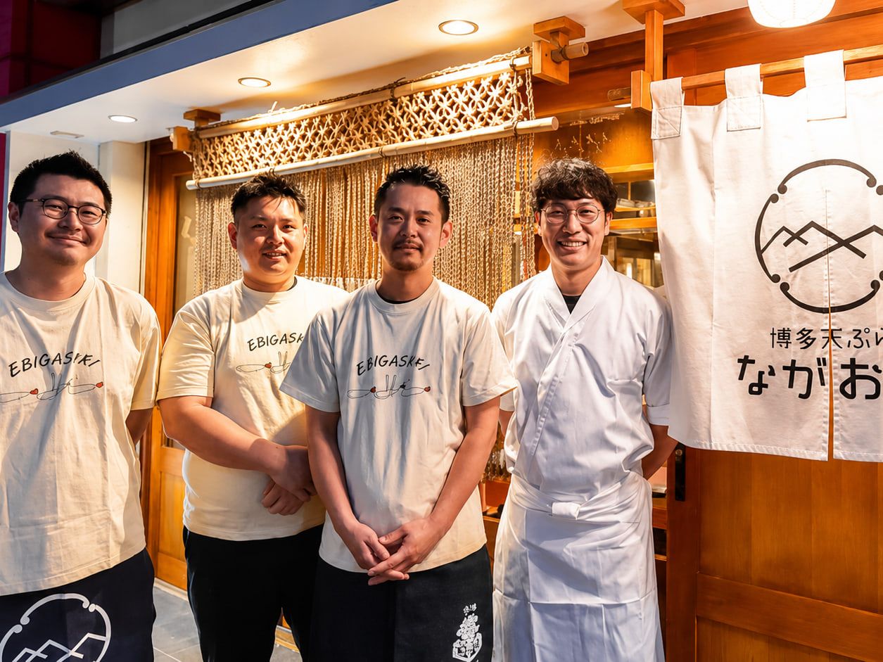のれんの前に並んで笑顔を見せる、博多天ぷら ながおか本店のスタッフ4人