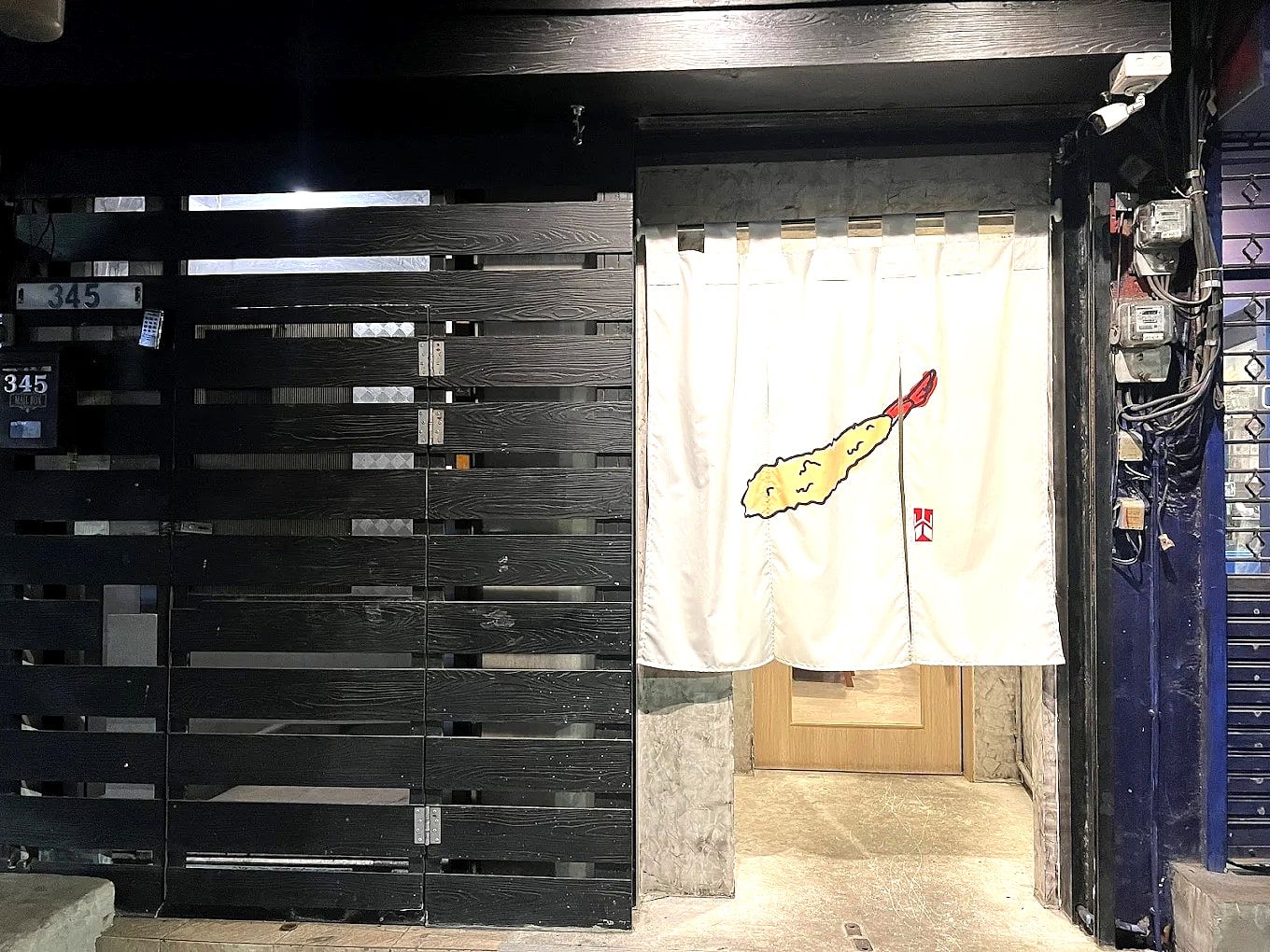 海老の天ぷらを染め抜いたのれんが掛かる、博多天ぷら ながおか バンコク エカマイ店の入口