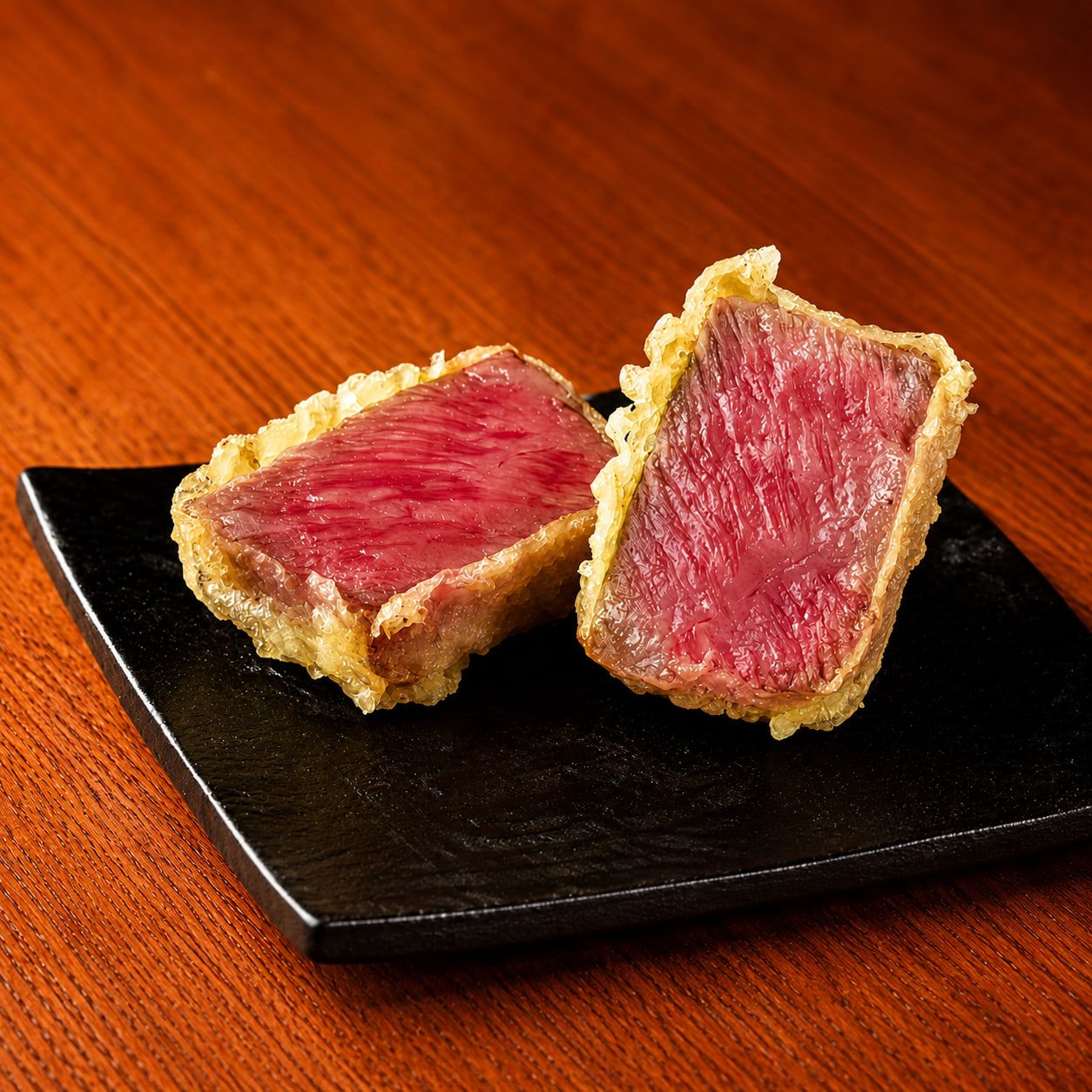 黒い角皿に盛られた和牛の天ぷら。断面はロゼ色に仕上がっている